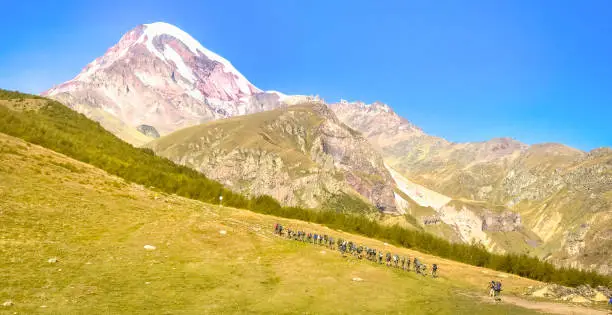 Guided group of mountaineers hiking up the hill with KAzbek mountain peak in the background. Kazbeki national park.