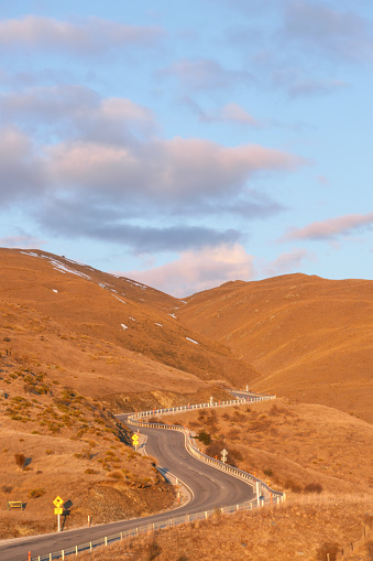 The Crown Range Road near Queenstown viewed from the Crown Range Scenic Lookout at sunset in early Spring.  The sign with yellow writing on the left of the road says 