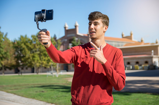 Portrait of businessman recording video presentation at smartphone with steadycam. Focused young man standing outside, holding steadycam while recording video presentation about new object