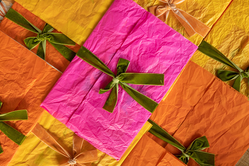 Multi-colored envelopes decorated with ribbons and bows are stacked together on the table, top view. Background image on a greeting and holiday theme