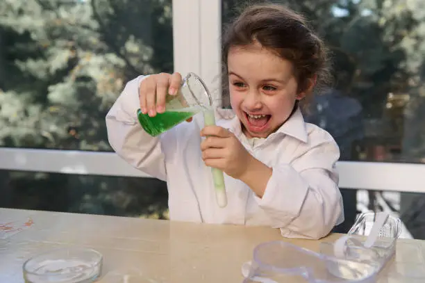 Photo of Mischievous little girl conducts chemical reactivity with citric acid soda, in school chemistry lab. Volcanic eruption