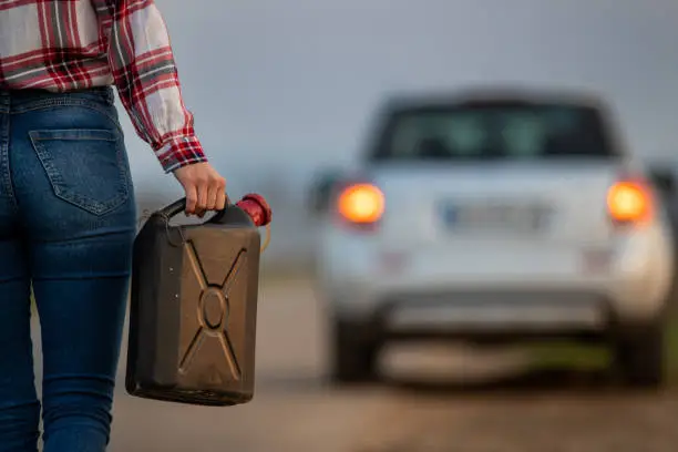 Close up of a woman holding fuel canister full of fuel to pour into her empty tank of car.