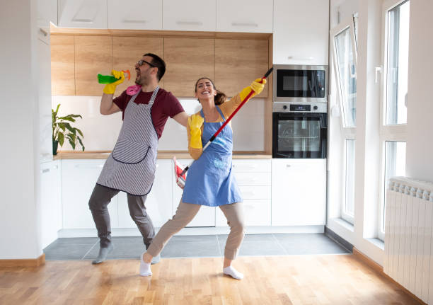 Cheerful couple dancing and singing while cleaning apartment together. stock photo