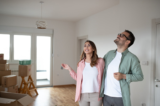 Young smiling couple looks around their new apartment and they look satisfied while the woman holds the keys in her hand