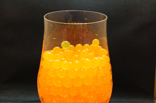 growing Orbeez in a glass. multicolored balls that grow in water from hydrogel. on a black background.