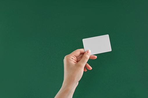Female Hand Holding White Credit Card Isolated On Green Background. Close Up. Christmas Gifts Buying. Chroma Key Screen. Woman's Hand with Plastic Gift Card MockUp. Advertisement gesture. 4K