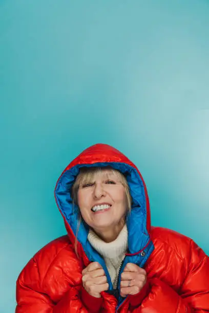Woman wearing a very highly insulated jacket against a cool blue background, the kind of clothing you see in Alaska and the Himalayas.