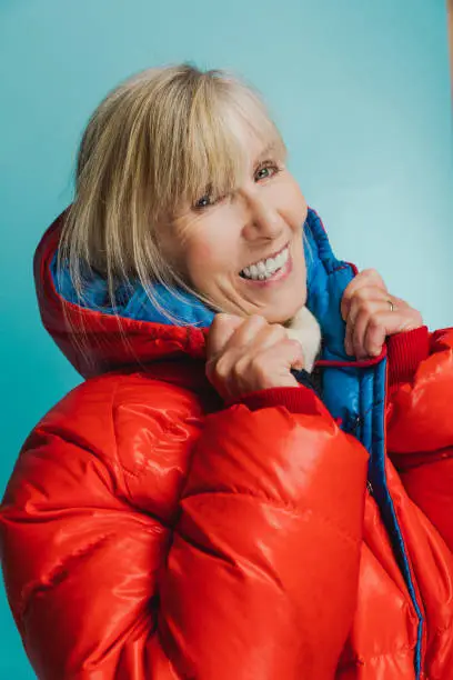 Woman wearing a very highly insulated jacket against a cool blue background, the kind of clothing you see in Alaska and the Himalayas.