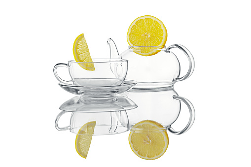 Still life of empty transparent cup and teapot with two bright lemon slices on top isolated on white background.  Studio shot, against the light.