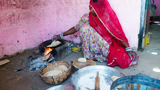 Bhinmal Rajasthan, India - May 23, 2017 : indian rural village woman preparing roti or chapatti food on traditional wood stove.