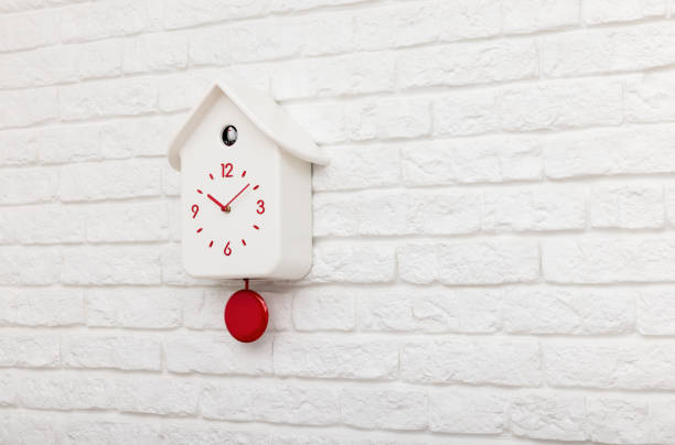 istock Cuckoo bird clock with red pendulum on a white brick wall 1429333630