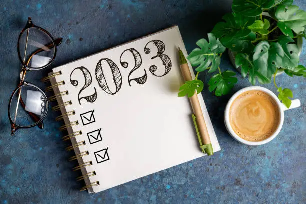 Photo of New year resolutions 2023 on desk. 2023 resolutions list with notebook, coffee cup on table. Goals, resolutions, plan, action, checklist concept. New Year 2023 template