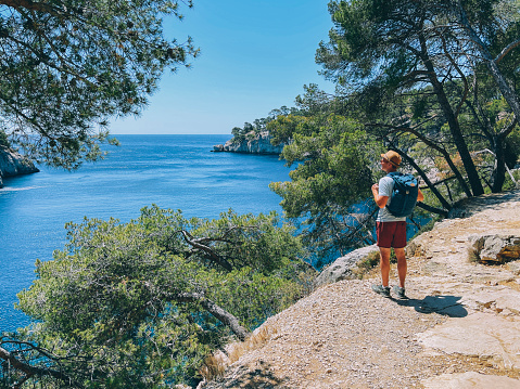 Young backpacker man with trekking poles enjoying the Mediterranean Sea on clifftop during Lycian Way trekking walk. Famous Likya Yolu Turkish route near Letoon. Active people vacations concept image