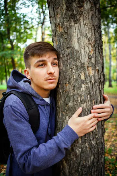 Young Man hug the Trunk of the Tree in the Forest