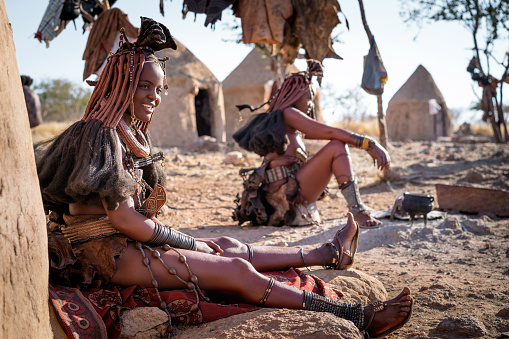 Himba women sitting outside their huts and dressed in traditional style in a Himba village near Kamanjab, Namibia, Africa.