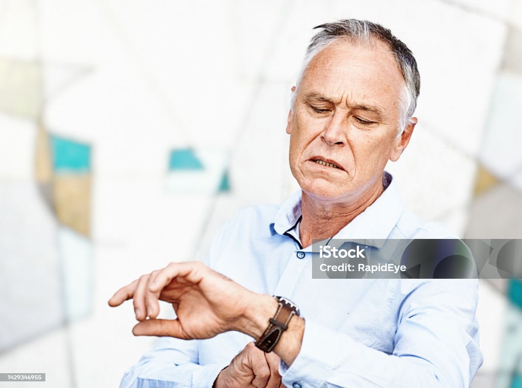You're late! Irritated middle-aged man checks the time on his wristwatch Handsome man, looking displeased, checks his watch. 50-54 Years Stock Photo