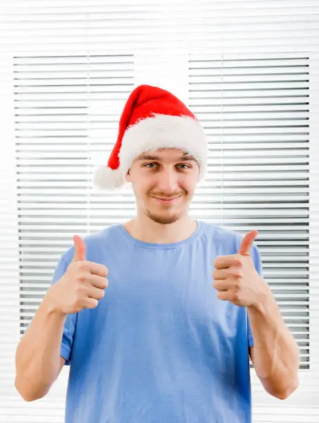 Young Man in Santa Hat with OK Gesture on the Jalousie Background