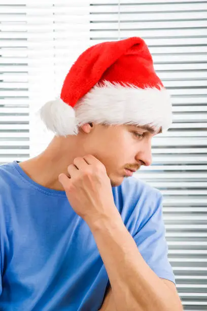 Pensive Young Man in Santa Hat on the Jalousie Background