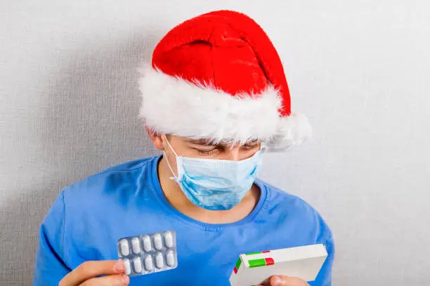 Young Man in Santa Hat and the Flu Mask with a Pills Pack
