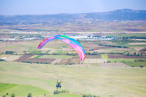 Against background of blue summer cloudy sky, tandem of paragliders flies on red ultralight aircraft - paraglider. Extreme sport and recreation.