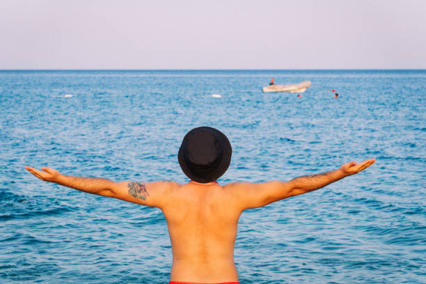 Young male photographer wearing a fedora taking pictures by the sea.