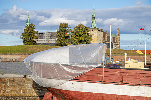 Elsinore, Helsingør, Denmark - September 6th 2022: Old lighthouse wooden ship with a tarpaulin over the front and a view to the tower of the famous Elsinore Castle also known as Kronborg