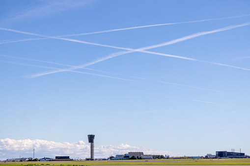 Copenhagen Airport, Copenhagen, Denmark - September 5th 2022: One of the control towers under a clear blue sky with jet vapor trails crossing each other