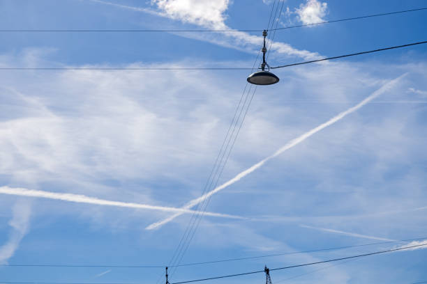Street lamp seen against a blue sky with clouds and vapor trails after jet planes