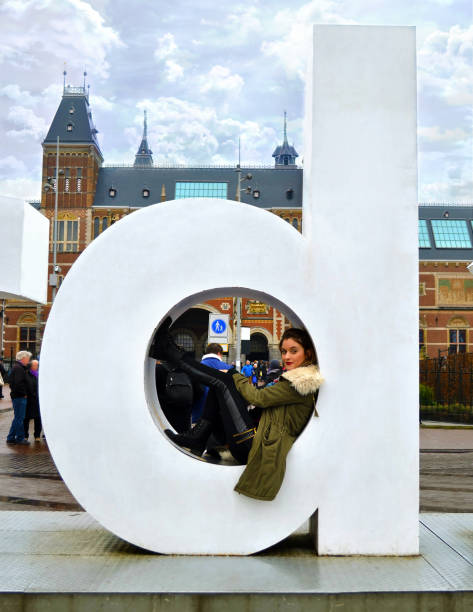 girl sitting on the popular ''I Amsterdam'' slogan in front of the Rijksmuseum in Amsterdam Holland stock photo