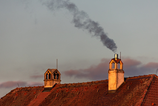 Old roof with a smoking chimney in the last evening sunlight.