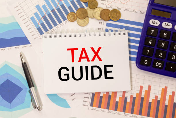 istock Calculator with text Tax Guide. Calculator, currency, book, bills and computer keyboard on bright background. 1429364232