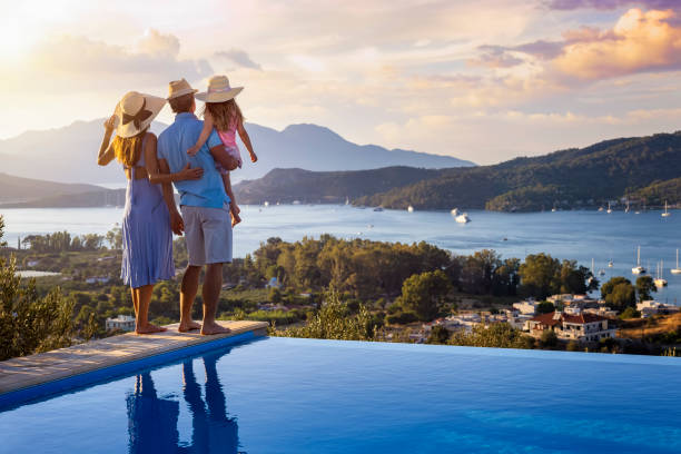 una familia en vacaciones de verano se para junto a la piscina y disfruta de la hermosa puesta de sol - holiday fotografías e imágenes de stock