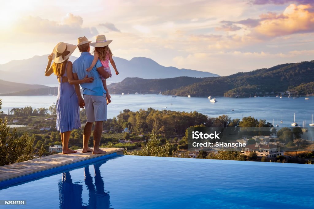 A family on summer holidays stands by the swimming pool and enjoys the beautiful sunset A family on summer holidays stands by the swimming pool and enjoys the beautiful sunset behind the mountains and the sea Vacations Stock Photo