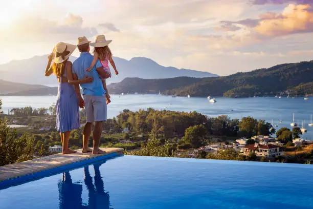Photo of A family on summer holidays stands by the swimming pool and enjoys the beautiful sunset
