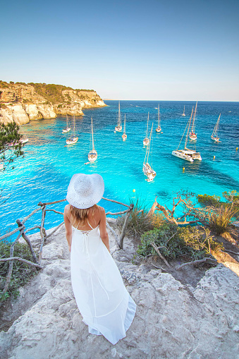 One woman with white dress and white hat in viewpoint between cala Macarella and cala Macarelleta the emblematic beach of turquoise colour water of mediterranean sea in Balearic island of Menorca