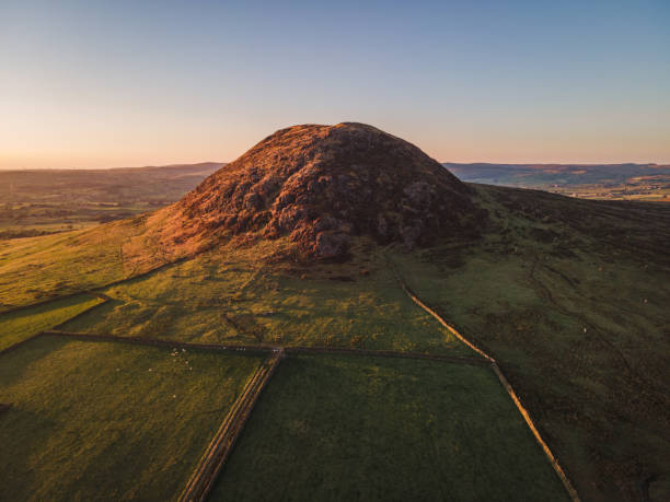 Slemish mountain tourist attraction in County Antrim, Northern Ireland, in summer Aerial drone view of Slemish mountain near Ballymena, County Antrim, Northern Ireland, on a summer evening at sunset, with beautiful side lighting and blue sky, it is a popular tourist attraction and hiking location, and St. Patrick tended sheep there as a young man extinct volcano stock pictures, royalty-free photos & images