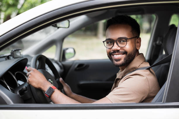 smiling young man driving a car - driver imagens e fotografias de stock