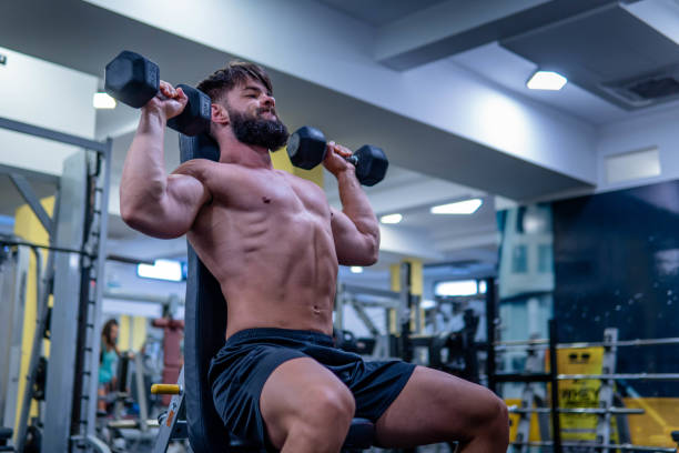Shirtless athletic man lifting dumbbells overhead Shirtless athletic man lifting dumbbells overhead, he is working out at the gym bodybuilder dumbell shoulder press