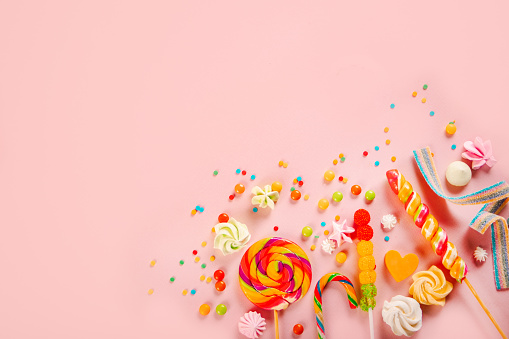 Top view of colorful candies and lollipops on pink background. Copy space