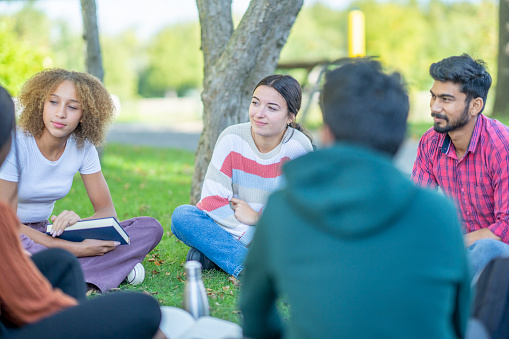 A small group of University students sit outside on campus as they take a break together between classes.  They are each dressed casually as they talk and catch up.