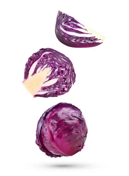 Photo of Whole red cabbage with slices falling in the air isolated on white