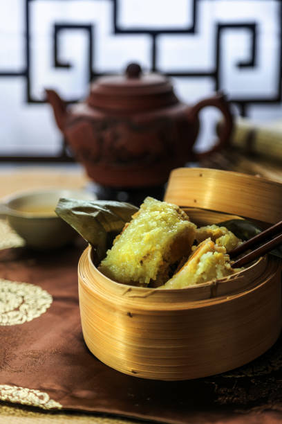 Closeup of rice dumpling zongzi cut open with chop sticks in steaming basket with tea set - Traditional sweet Chinese food on a plate for Dragon Boat Duanwu Festival celebration