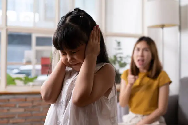 Photo of Indoor shot of young Asian girl crying and cover her ear with hands and feel sad while get scold and shout with angry from her angry mother. Child abuse that can cause a problem for children.