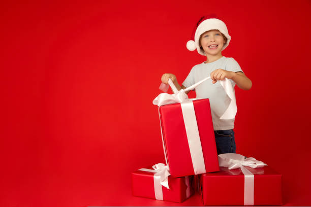 istock joyful boy in a red cap holds a festive bow on a large beautiful gift box 1429403249