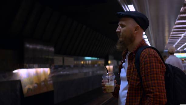 istock A bearded man in a cap stands on a subway platform and drinks iced coffee while waiting for a subway train. A typical day on the subway, a man goes to work every day early in the morning. 1429415398