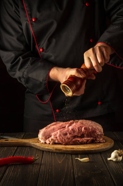 le chef prépare de la viande de veau crue. avant la cuisson, le chef ajoute du poivre au bœuf. le plat national est préparé dans la cuisine - veal calf meat baking photos et images de collection