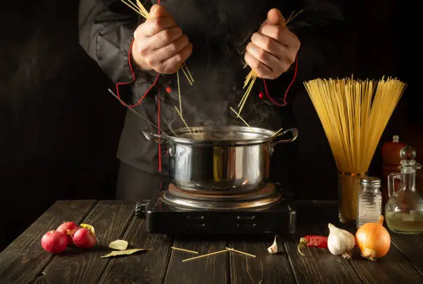 Chef prepares Italian pasta in a saucepan with vegetables. Close-up of cook hands while cooking in kitchen. Cucina italiana