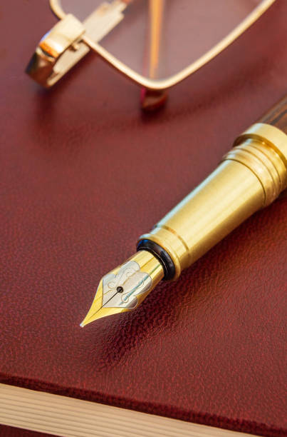 istock Stylish pen with a gold plated pen and glasses on brown notepad for notes 1429421565