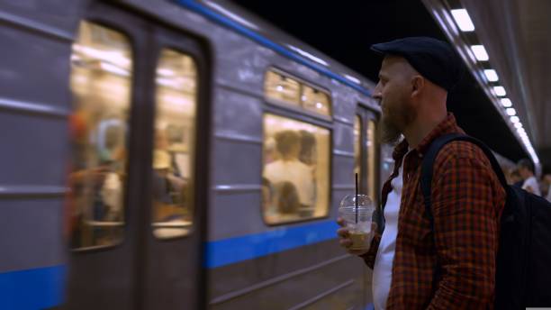 istock A bearded man in a cap stands on a subway platform and drinks iced coffee while waiting for a subway train. A typical day on the subway, a man goes to work every day early in the morning. 1429424554