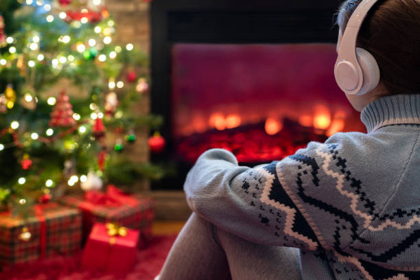 femme triste seule dans des écouteurs assise et se réchauffant le soir d’hiver près de la flamme de la cheminée et du sapin de noël. - tree house audio photos et images de collection